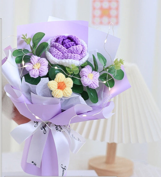 Bouquet of flowers wrapped in purple paper with a white ribbon, on a light background.