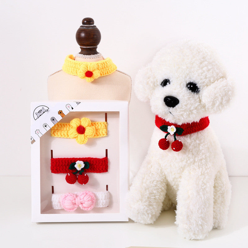 White teddy bear wearing a red crocheted collar with a white box containing yellow, red, and pink crocheted accessories on a white background.