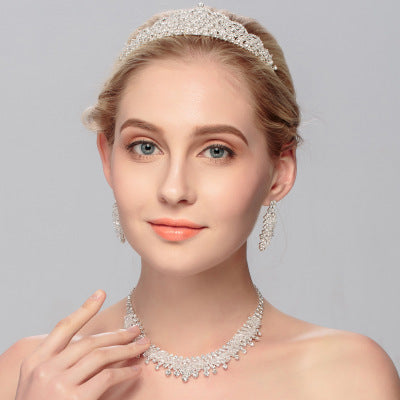 Woman wearing a diamond tiara, necklace, and earrings on a gray background