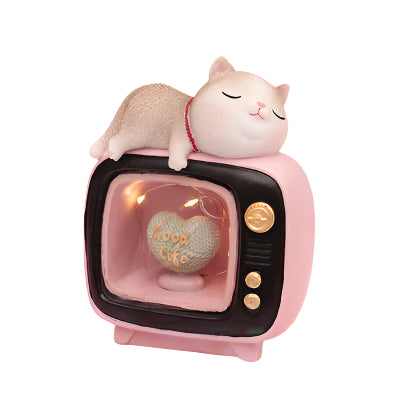 Small TV figurine with a cat on top against a pink background