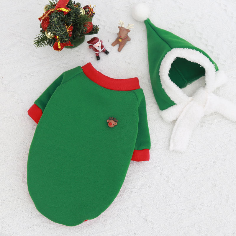 Green and red baby outfit with hood on a textured white surface, Christmas decorations in the background.