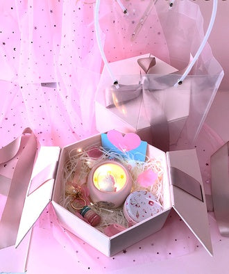 Decorative gift box with a candle and small toys on a pink polka dot background