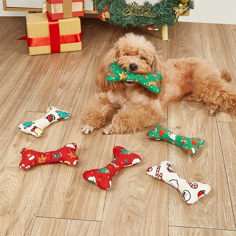 Dog playing with a green bone-shaped toy on a wooden floor with Christmas decorations.