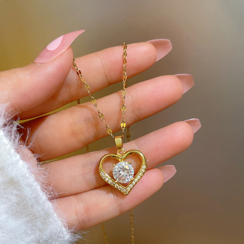 Gold heart-shaped necklace with a diamond pendant held by a hand against a blurred background