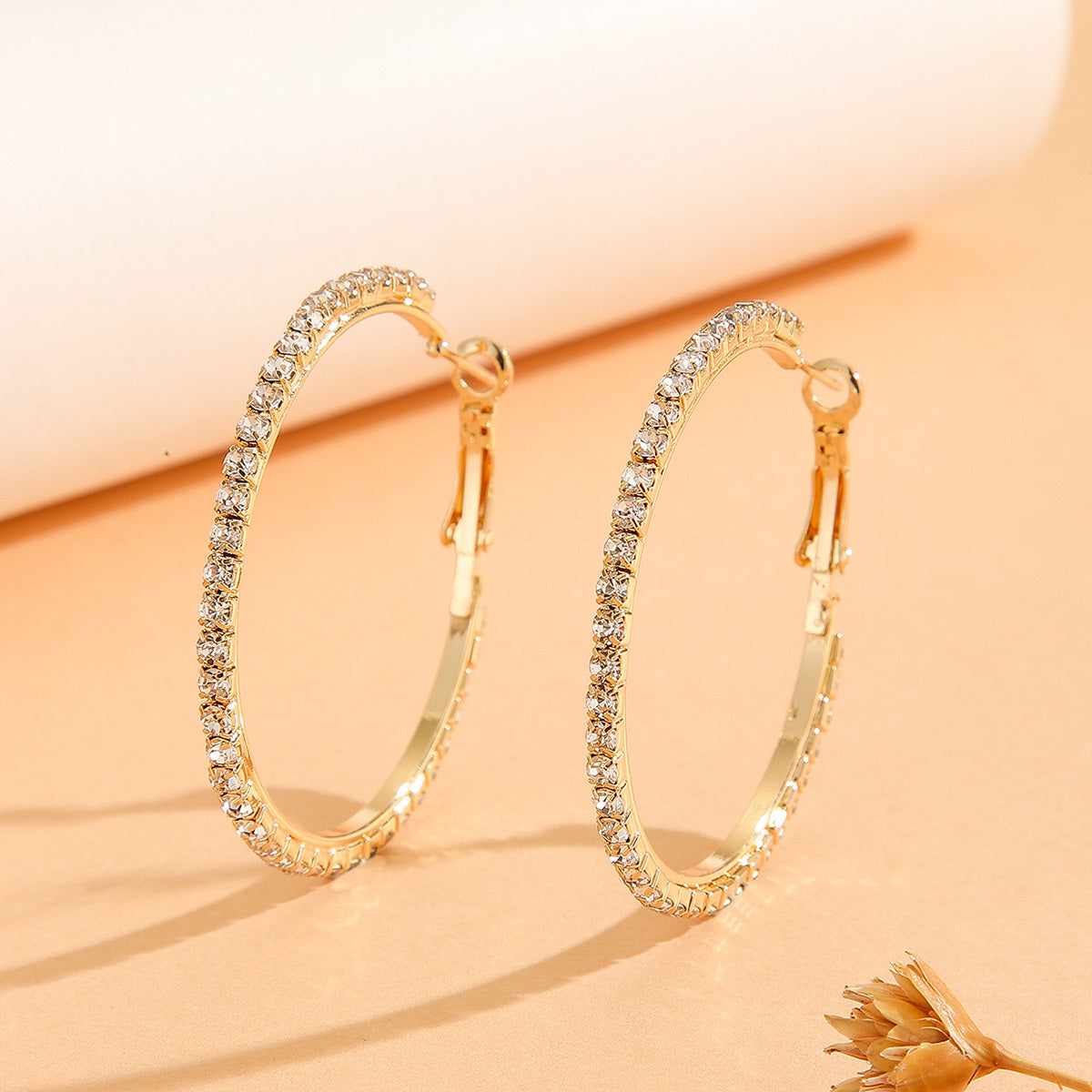 Gold hoop earrings with clear gemstones on a beige background