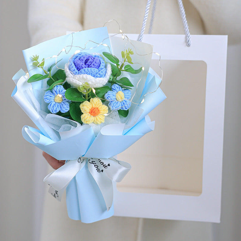 Bouquet of crocheted flowers in blue, yellow, and green with a white card on a light background