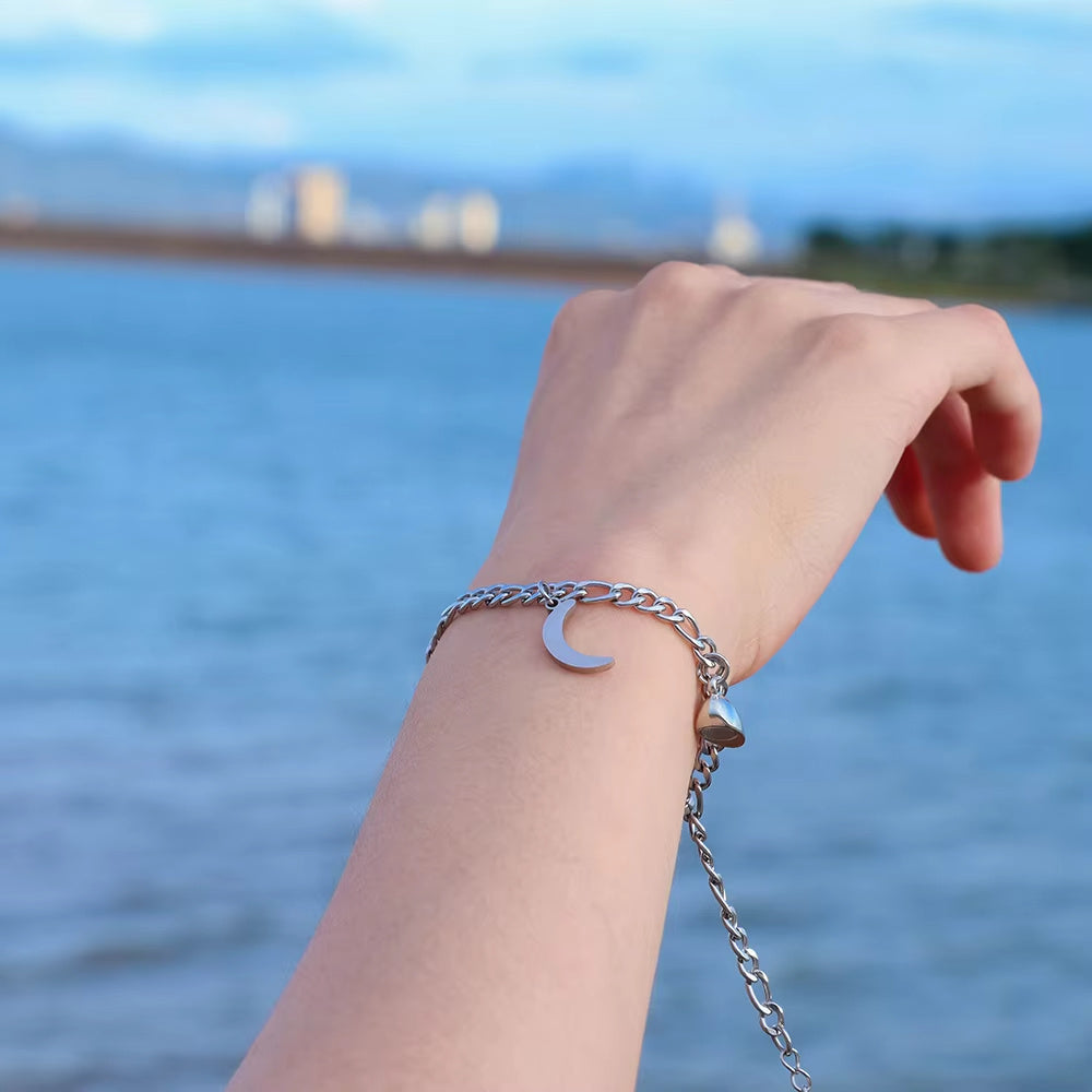 Hand wearing a silver bracelet with a moon charm against a blurred water and sky background