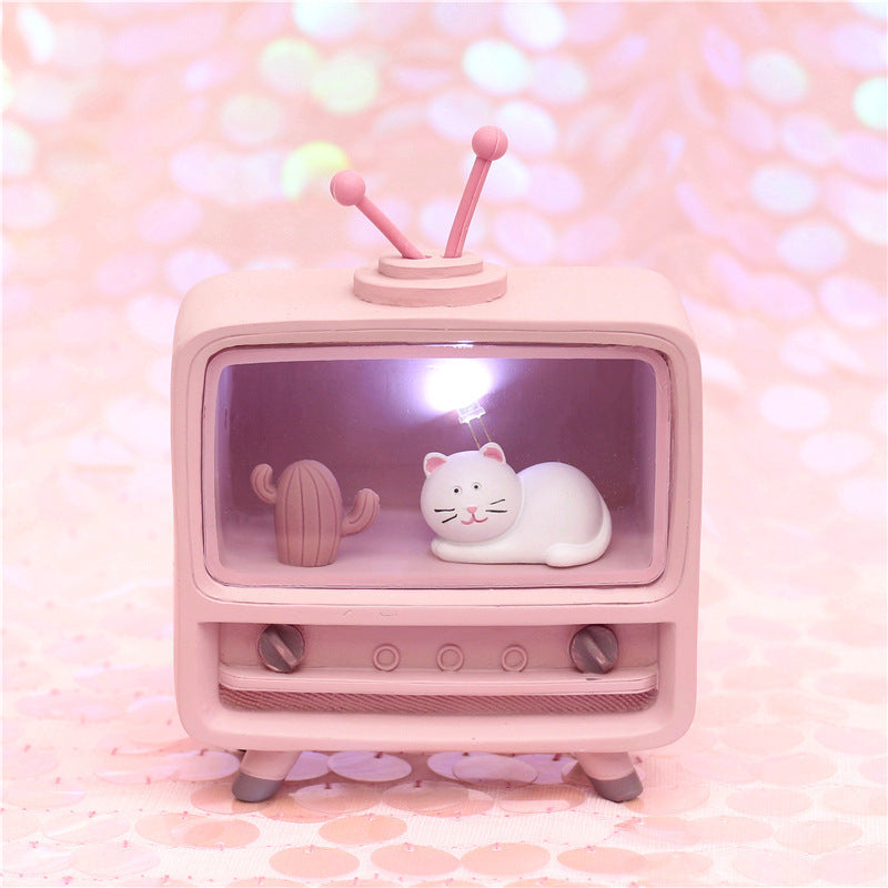 Small pink television set with a cat figurine on a pink background