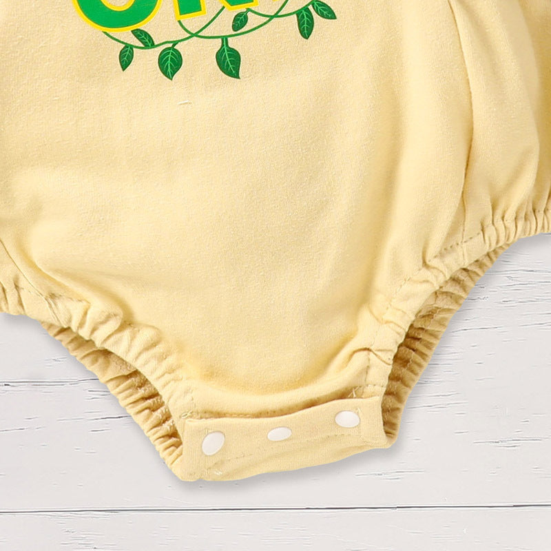 Yellow baby romper with green text and leaves on a light wooden surface