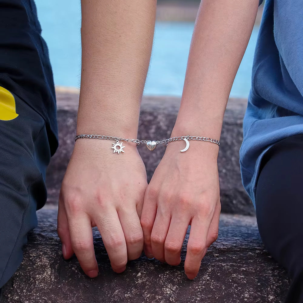 Two people holding hands with silver bracelets featuring sun and moon designs against a natural background.