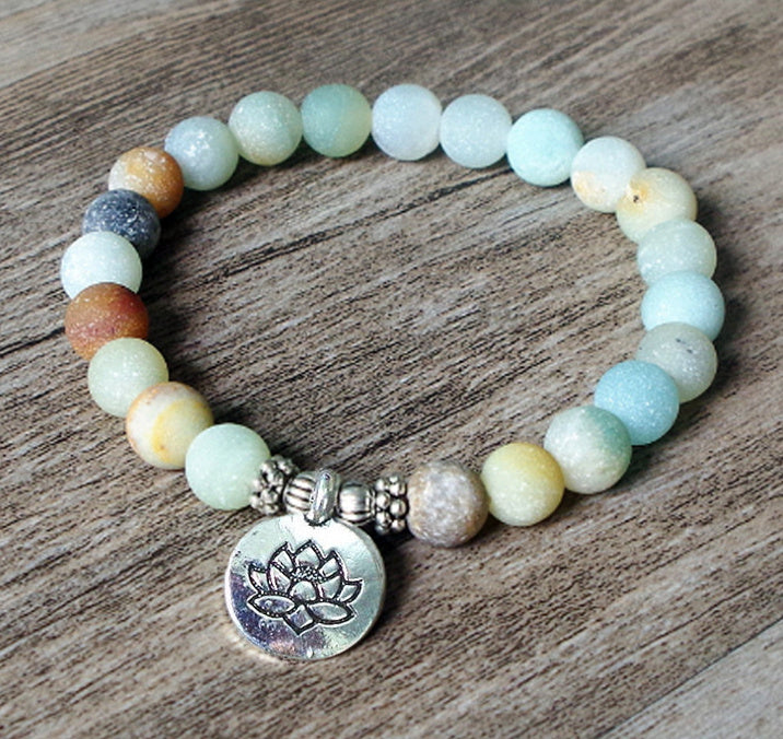 Multicolored beaded bracelet with a silver lotus charm on a wooden surface