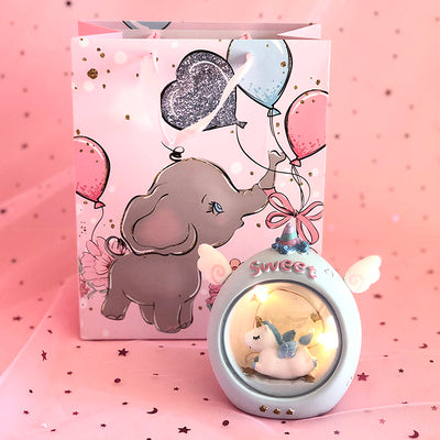 Decorative item with elephant design and glowing unicorn inside, on a pink background.