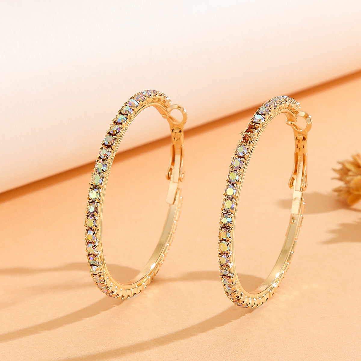 Gold hoop earrings with gemstones on a beige background