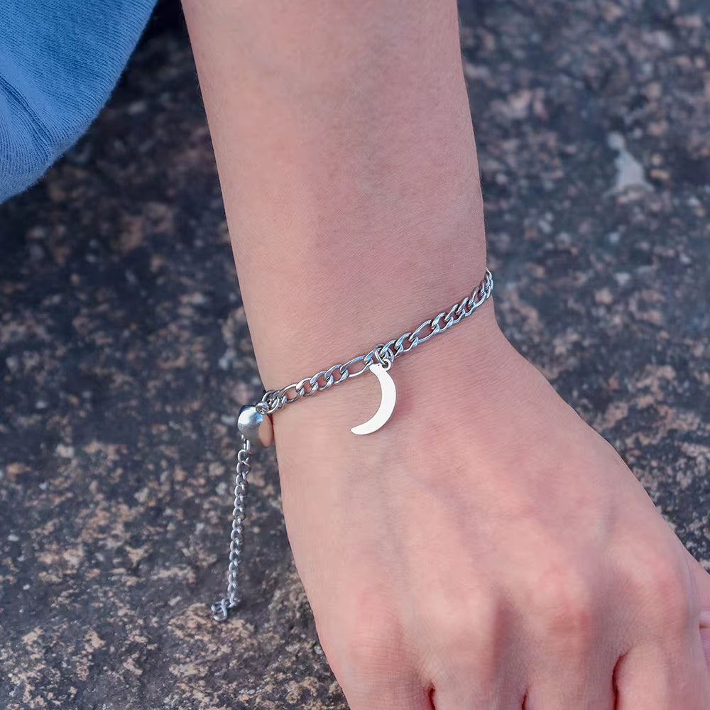 Silver chain bracelet with a moon charm on a wrist against a stone background