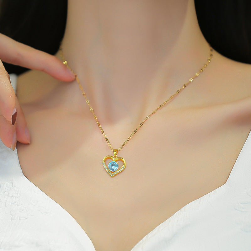 Gold necklace with a heart-shaped pendant featuring a blue gemstone on a mannequin.