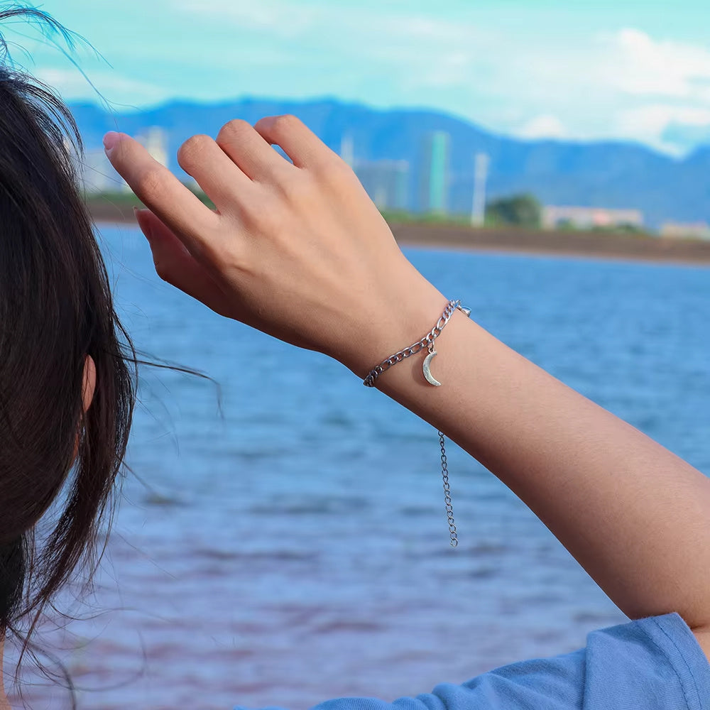 Person wearing a silver bracelet with a moon charm by a body of water