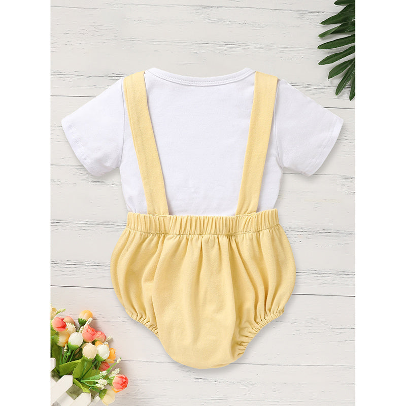 Baby romper with white shirt and yellow overalls on a light wooden surface.