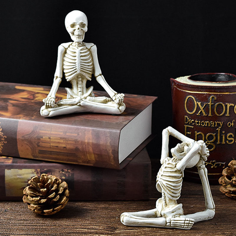 Two skeleton figurines in yoga poses on books with a dark background